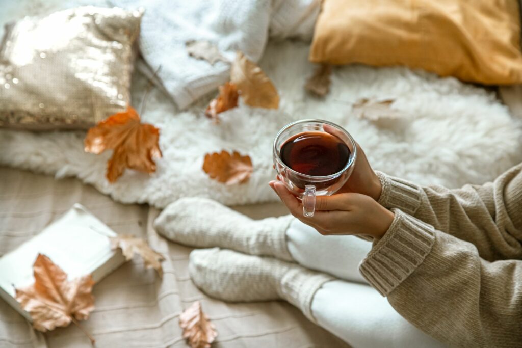 Photo of someone holding a coffee cup with autumn leaves, stay warm by investing in new insulation for your home