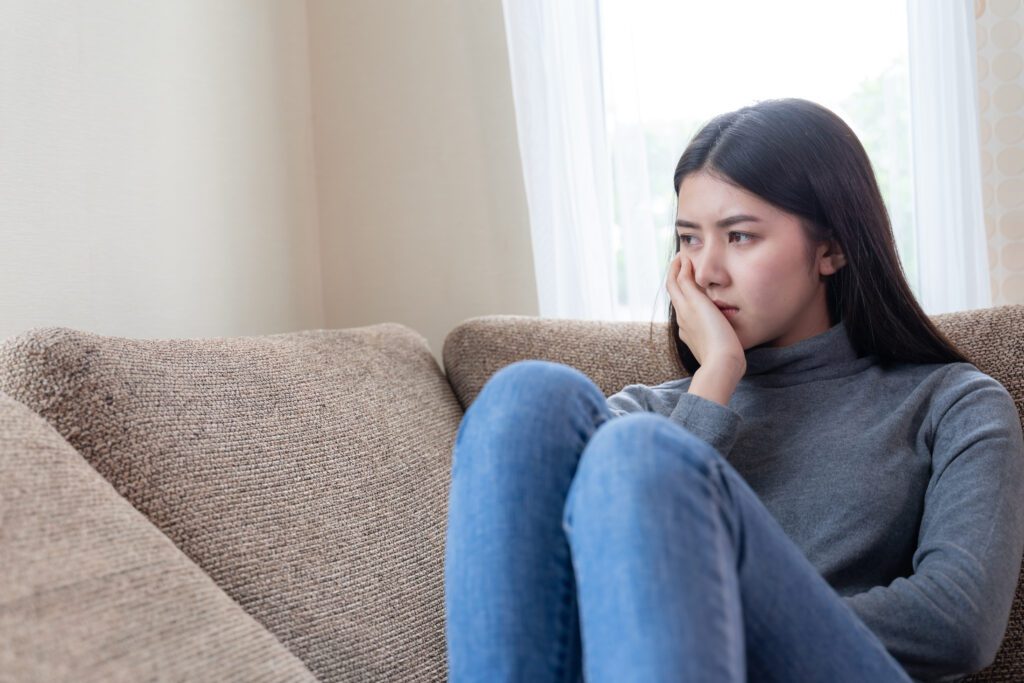 Women sitting on couch thinking of the consequences of dirty and bad home insulation she needs to replace