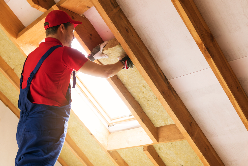 Man installing insulation batts in attic