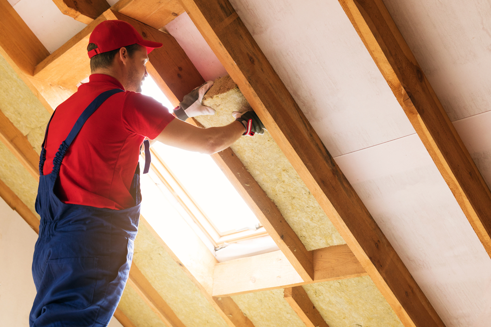 Image of a technician installing fiberglass batts during the best season to get new insulation